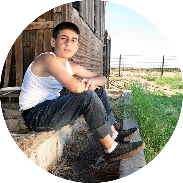 Teen boy in a white tank top and jeans sits on a concrete ledge