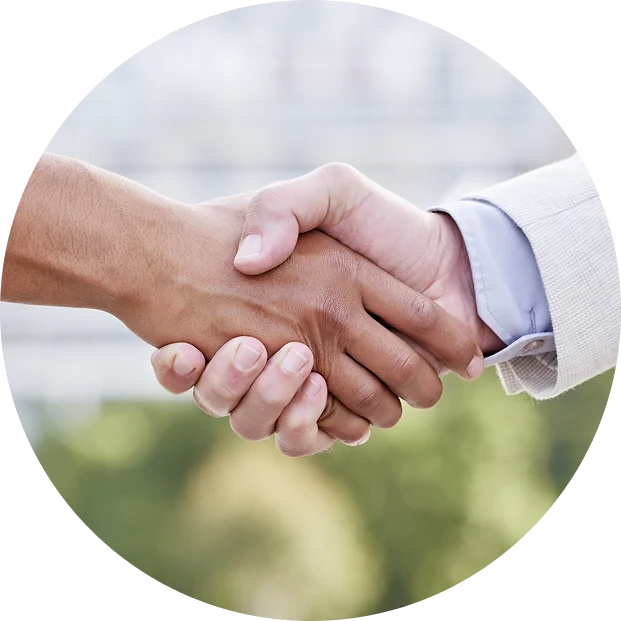 Two people shaking hands outdoors, one wearing a light-colored suit jacket and the other with a darker skin tone, against a blurred background.